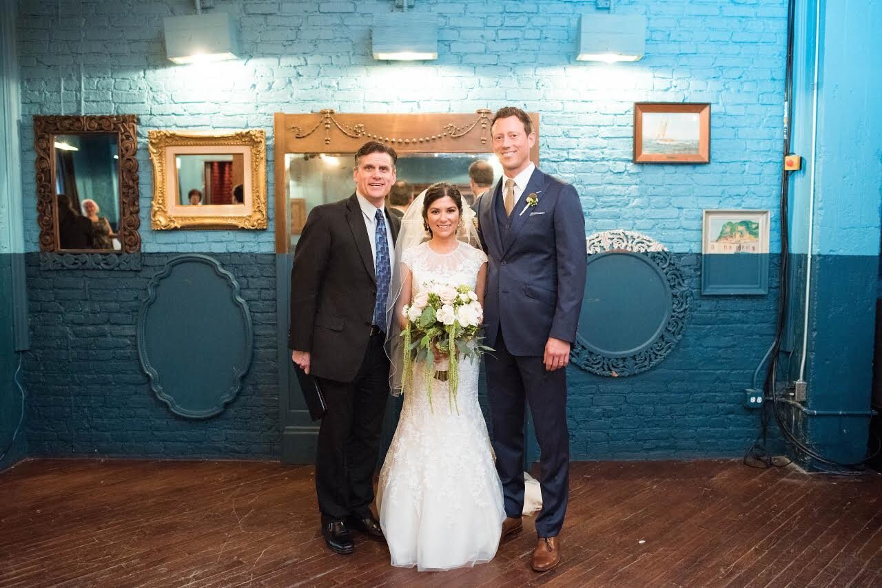 Bride and groom smile with their wedding officiant after wedding ceremony