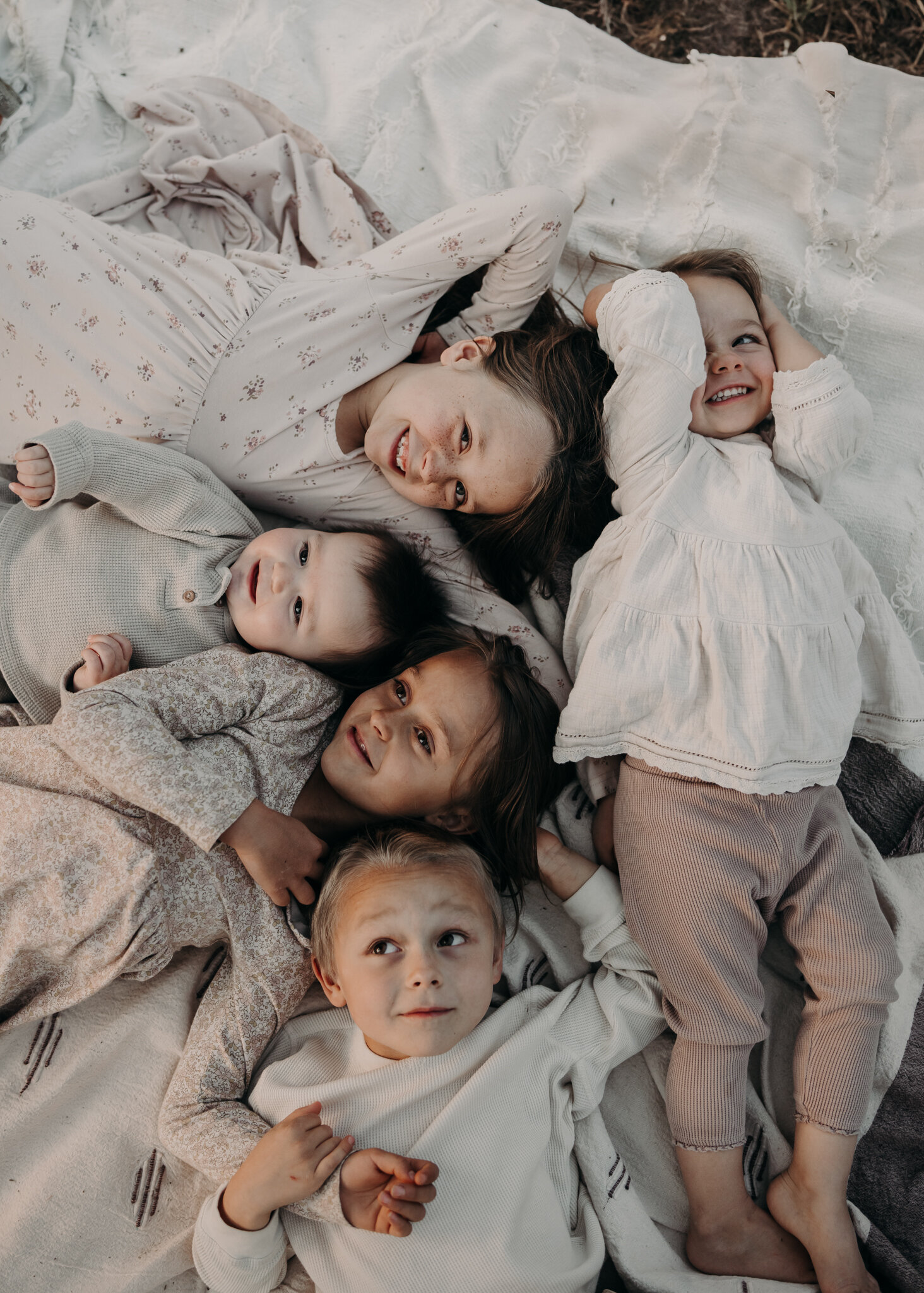 Four siblings casually lay with their heads together on a blanket, while giggling and smiling together.