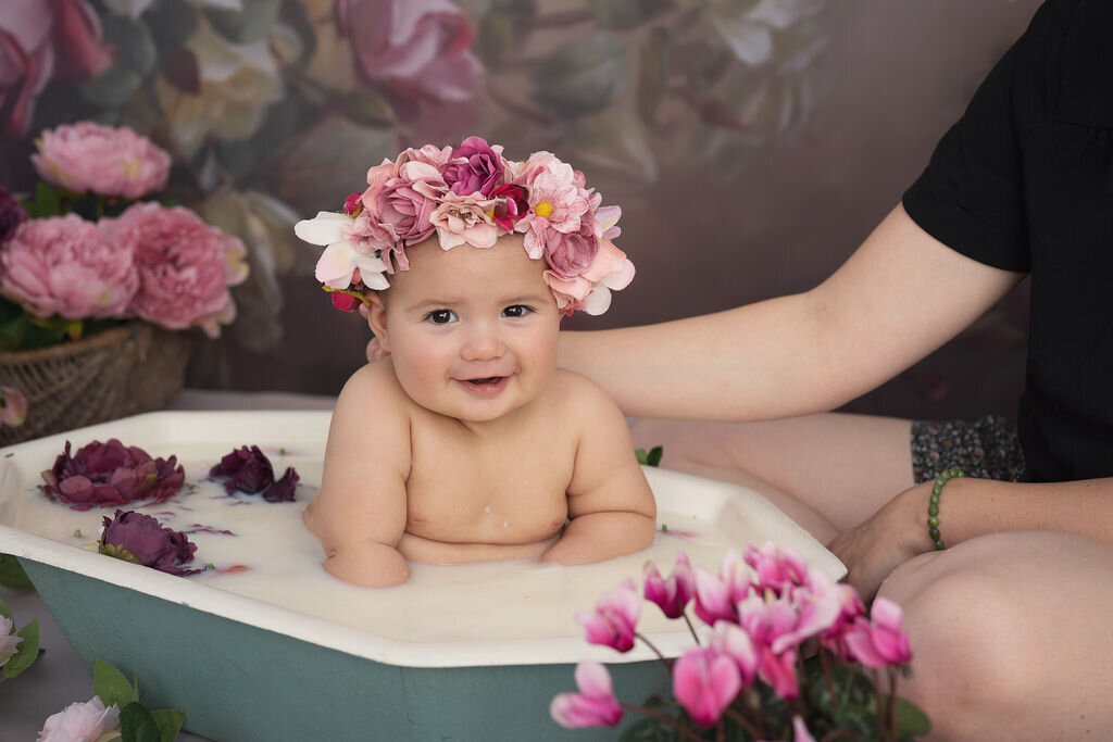beautiful baby girl in a milk bath with flowers all around