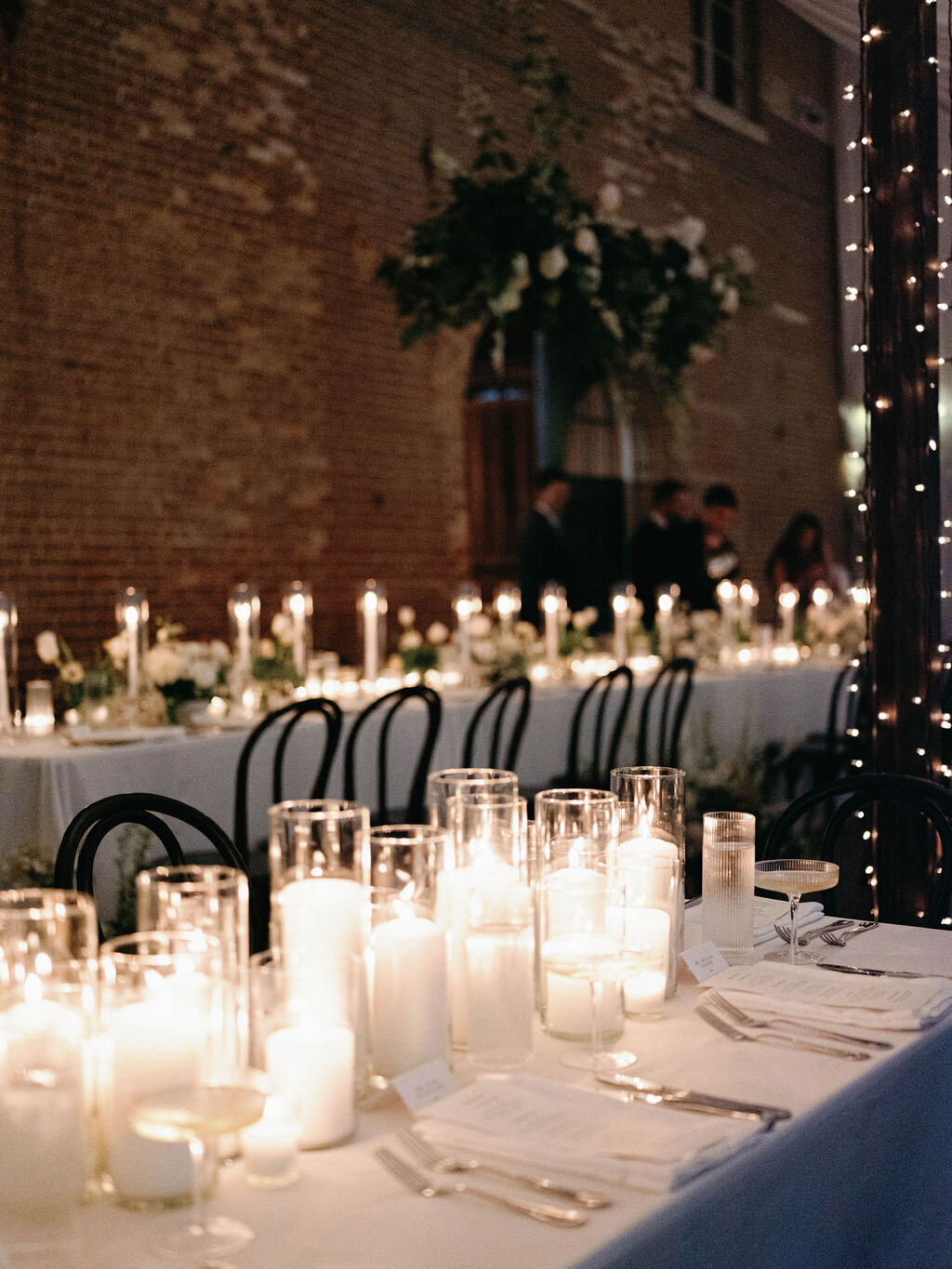 Long guest tables at the receptions at the Evergreen Museum Carriage House with an abundance of ivory pillar candles and hanging installation over the head table.