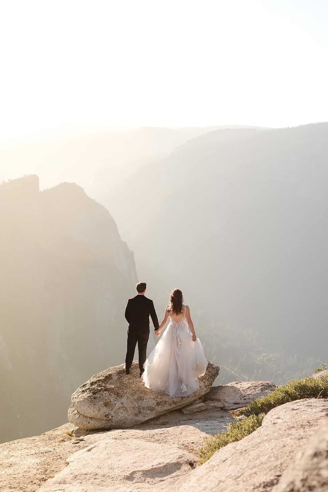 A bride and groom wait for sunset on their Yosemite Elopement day from the epic view at Taft Point in Yosemite National Park.