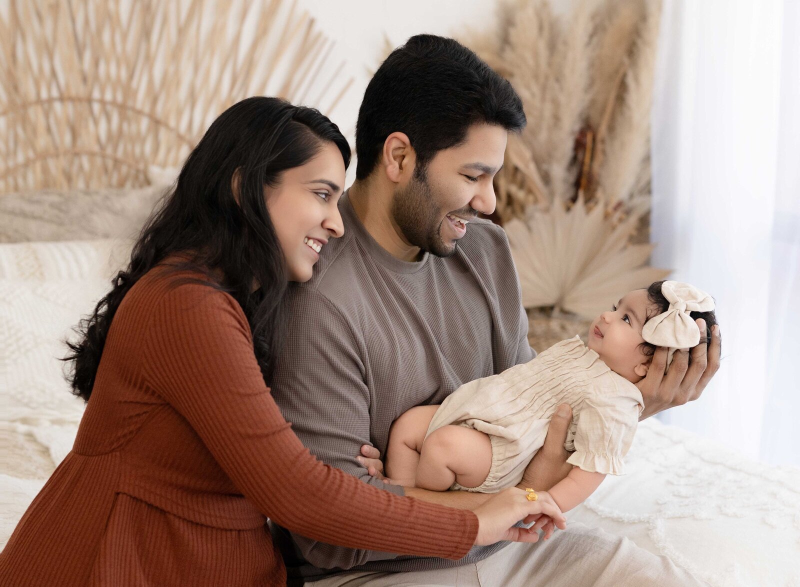 Boho styled bedroom with mom and dad on bed looking at their baby girl. Baby milestone photo taken by Jenni Nikki Photography in Atlanta, GA. 
