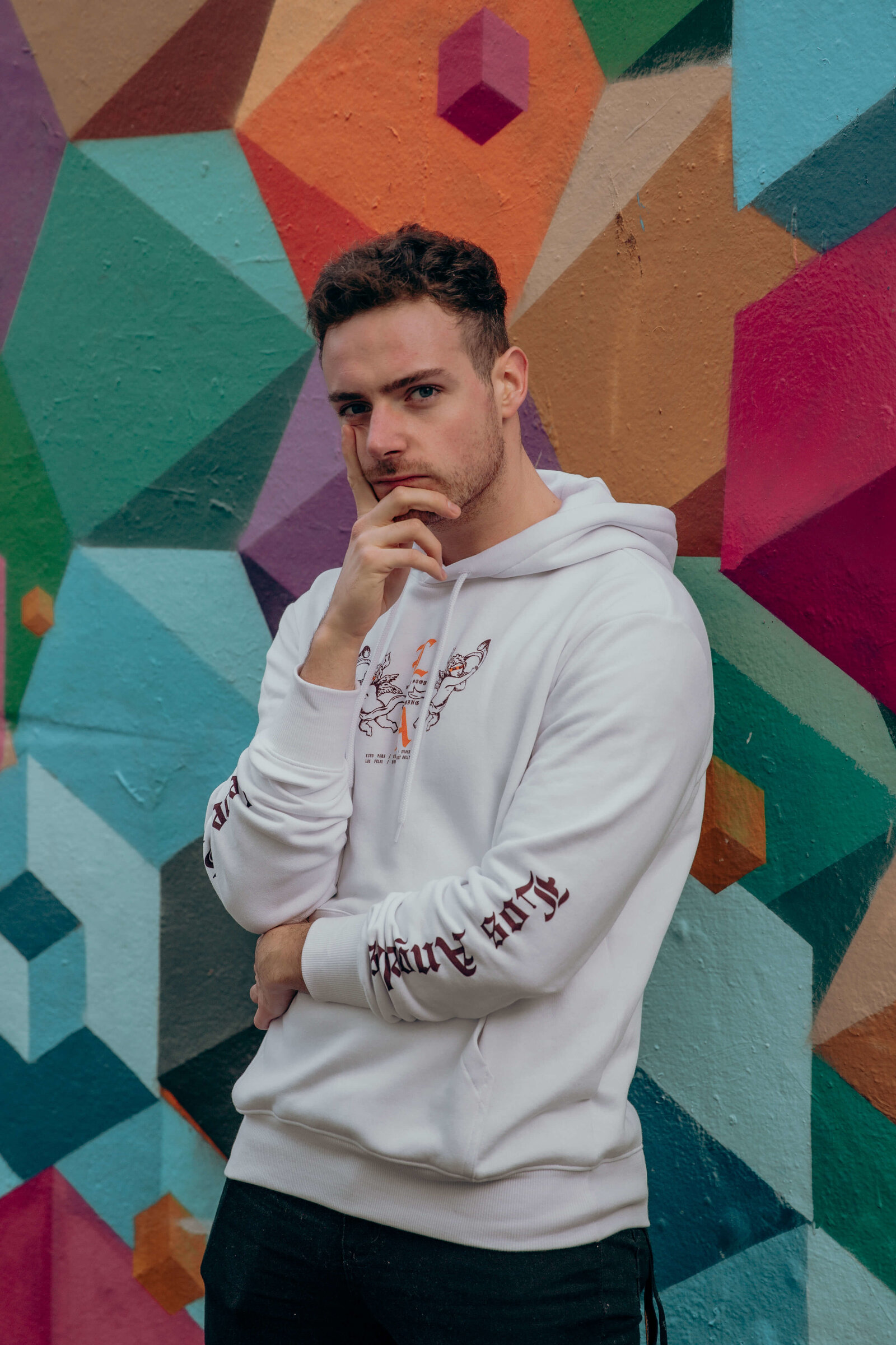 Connor stood leaning against a wall covered in colourful graffiti.