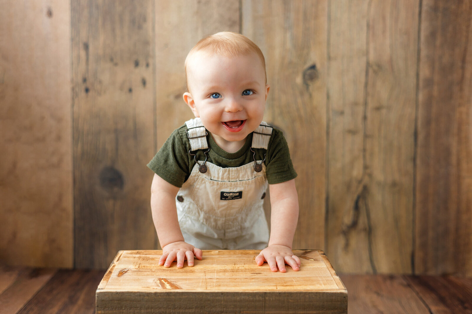 8 month old wearing an overalls standing and leaning on a create at Constance Calton photographery's studio in Guyton, ga