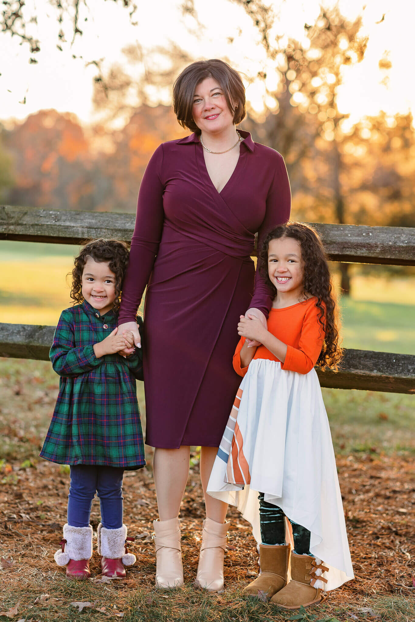 A mom and her two little girls standing up against a fence