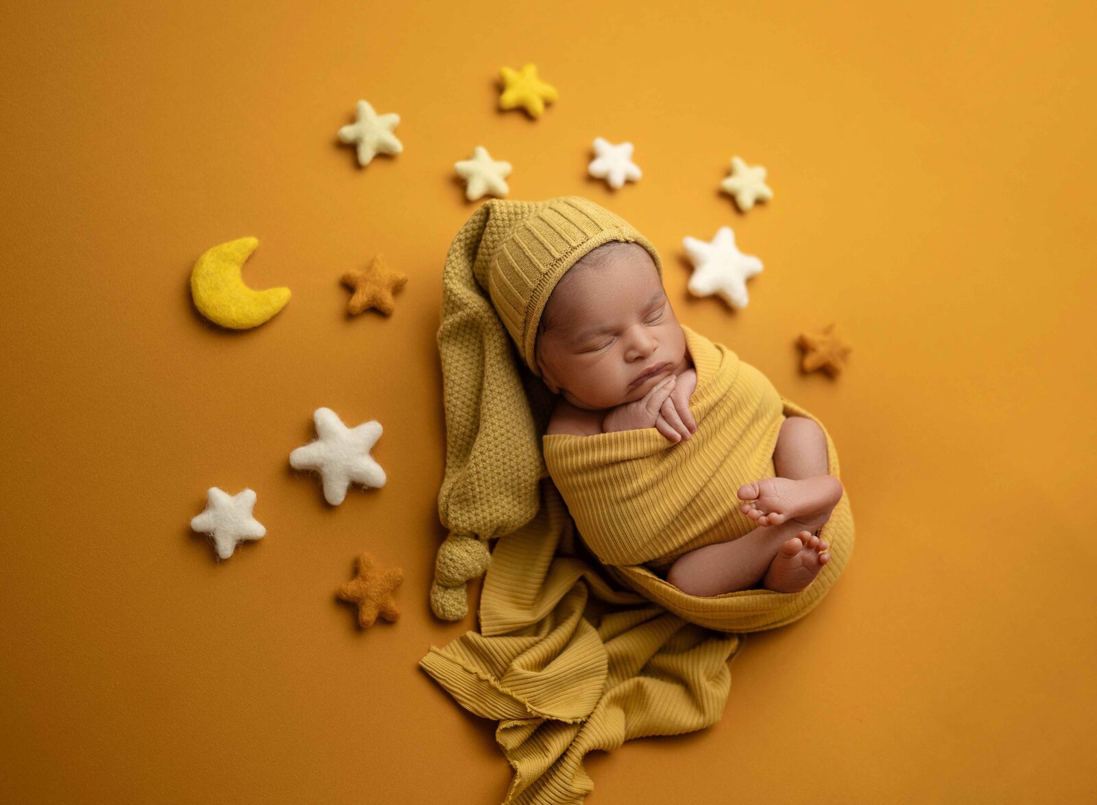 Baby wrapped in a mustard yellow swaddle with felted moon and stars around him. Photographed by Atlanta baby photographer, Jenni Nikki Photography.