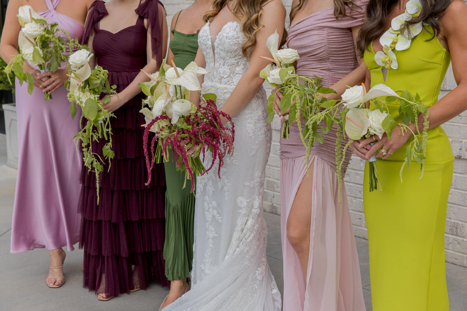 A groom holds the train of his bride's dress as the walk away from the camera. Behind them is  white house.