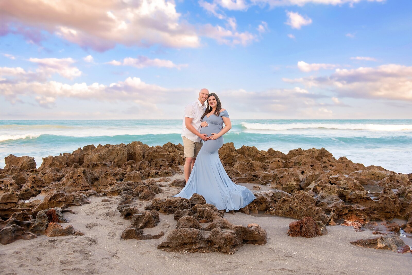 Pregnant wife happily posing with her husband on the beach for their maternity photoshoot at sunset in Jupiter, FL.