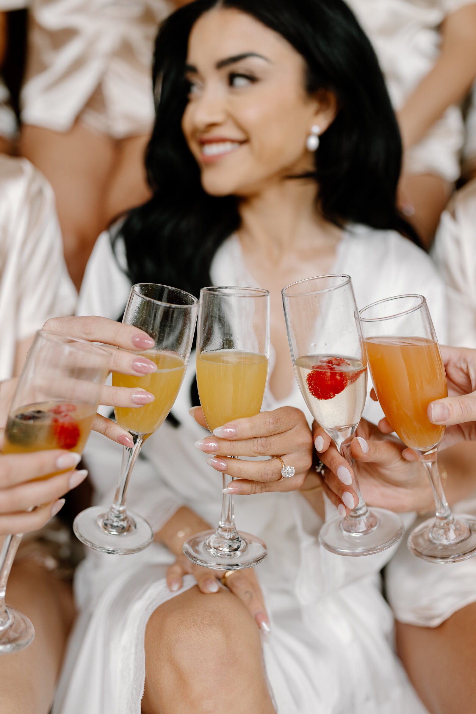 Bride and bridesmaids raising glasses of mimosas, celebrating the wedding morning before hair and makeup by Promise Artistry.