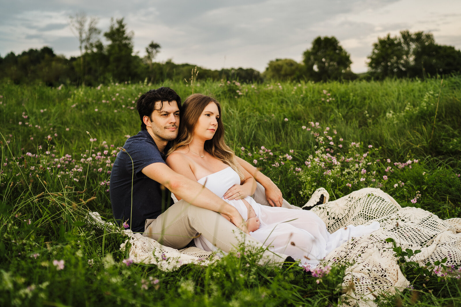 pregnant couple sits in field of flowers