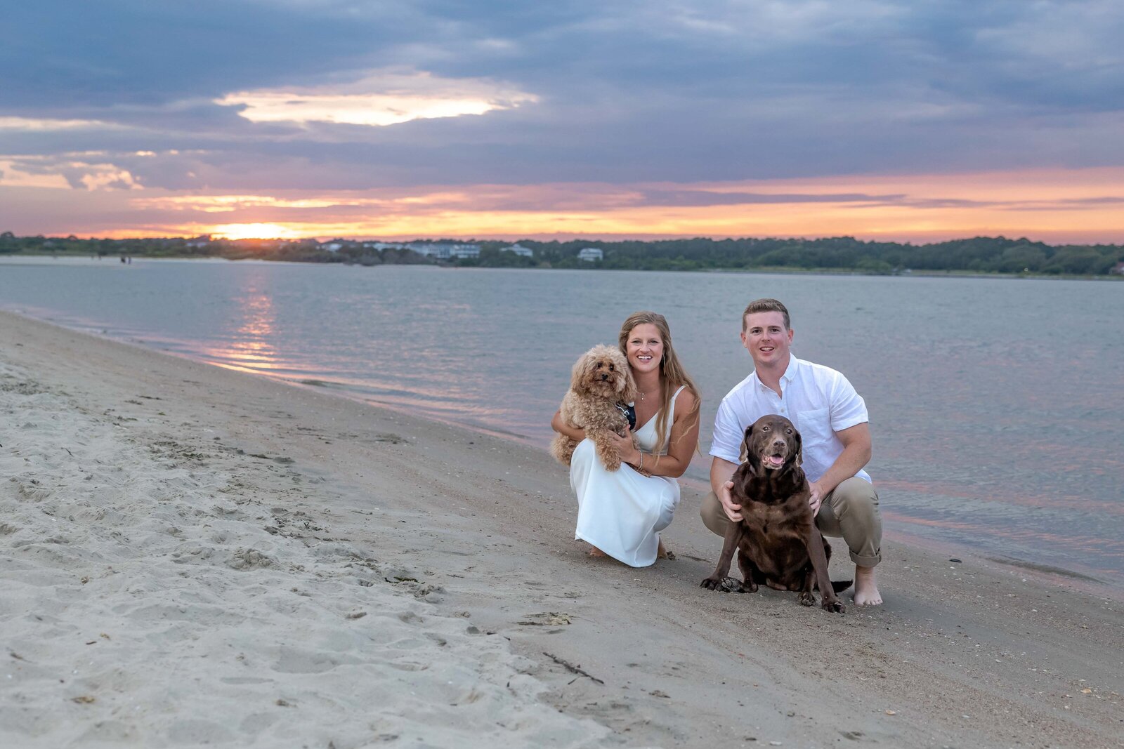 A couple poses with their two dogs on the beach at sunset during an engagement session in Wrightsville Beach, NC, blending authentic moments with coastal beauty and pet-friendly charm.
