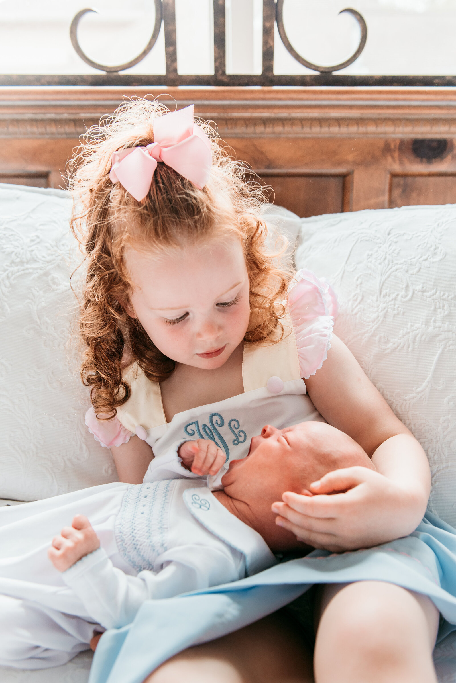 big sister holds her newborn brother while he yawns and she looks in admiration at him