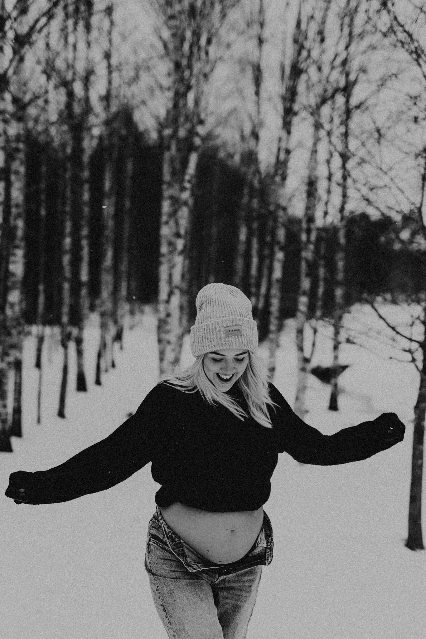 en gravid mamma springer snö iklädd jeans och luvtröja