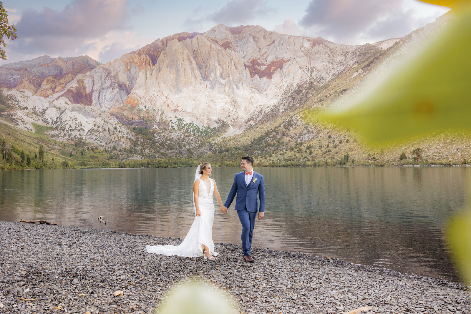 Bride and groom hold hands and walk in front of Mammoth Lake while smiling. Photo by Wedding photography studio Sacramento, CA, Philippe Studio Pro.