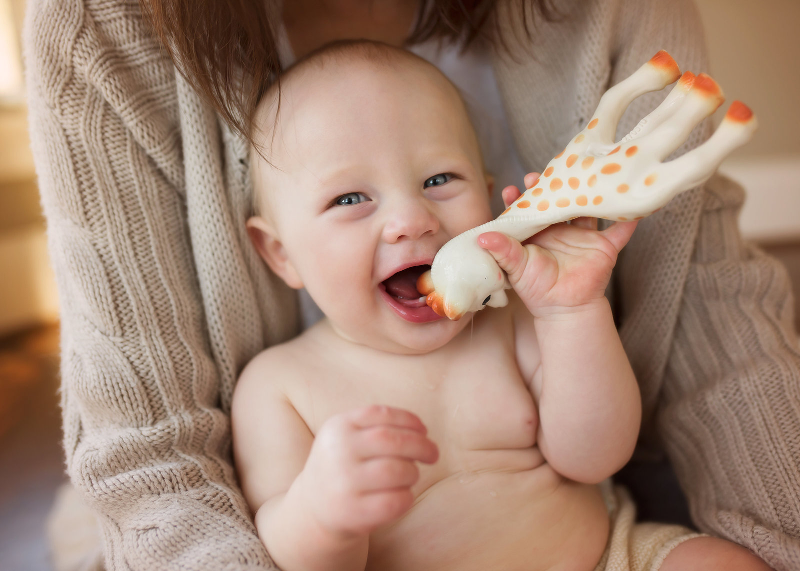 baby boy laughing in mom's lap with sophie giraffe toy in mouth