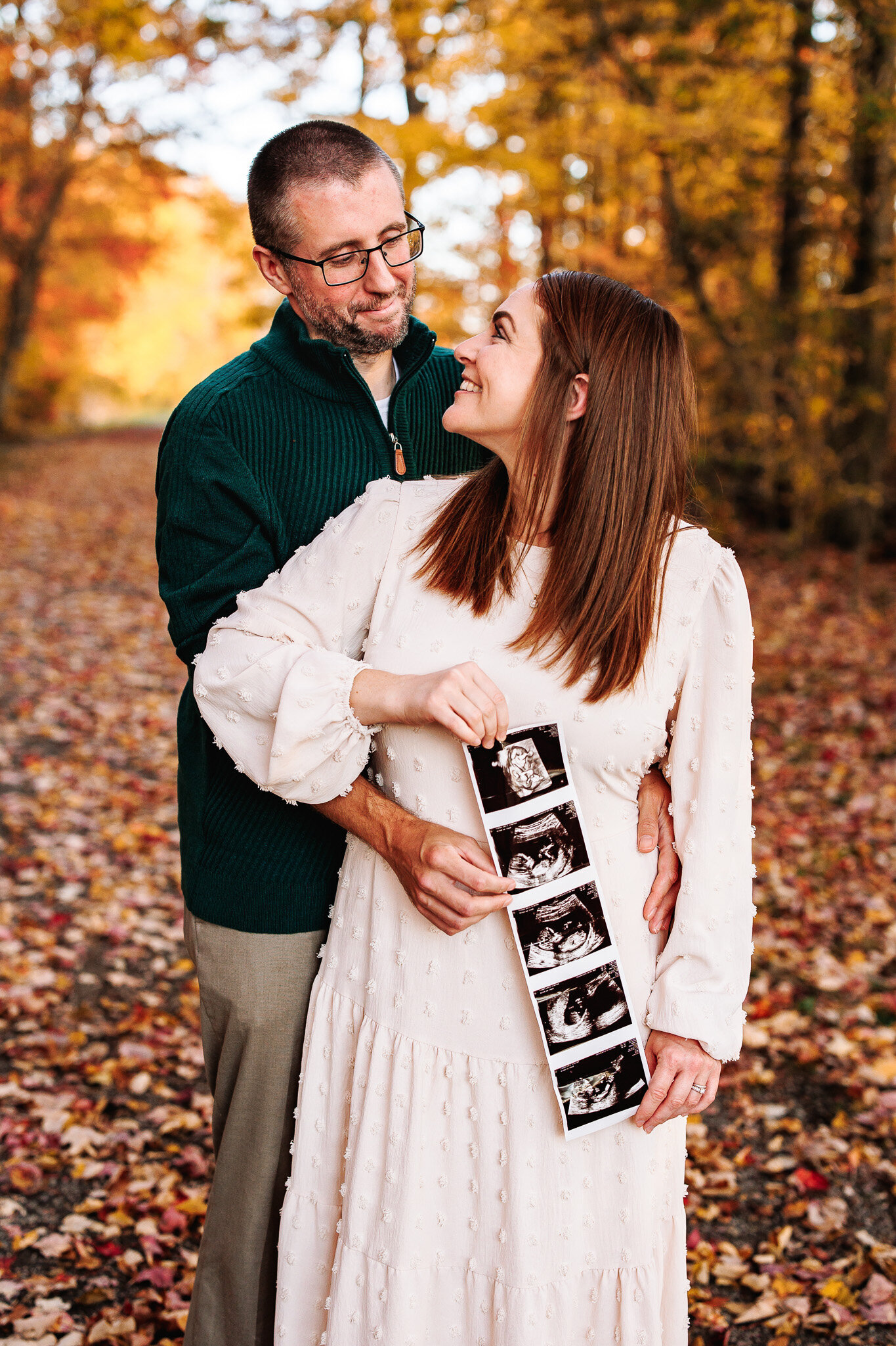 Holding their sonogram photos, a couple gazes at each other amongst fall foliage