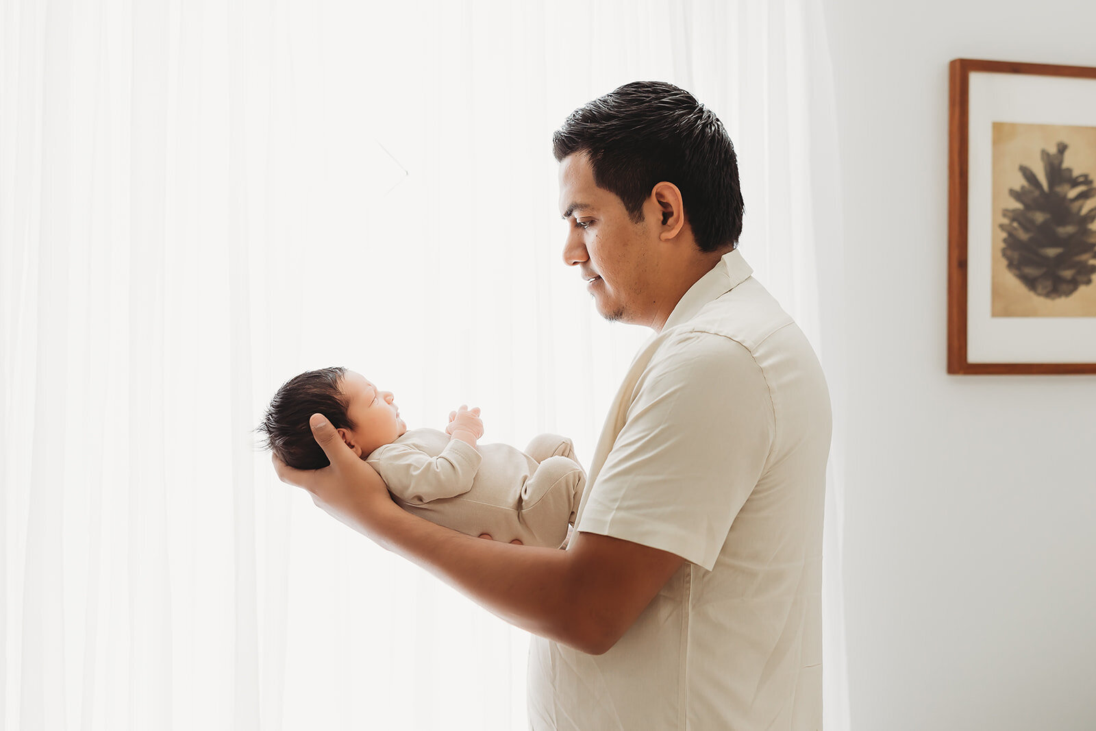 Dad holding his newborn baby boy standing in front of a bright window