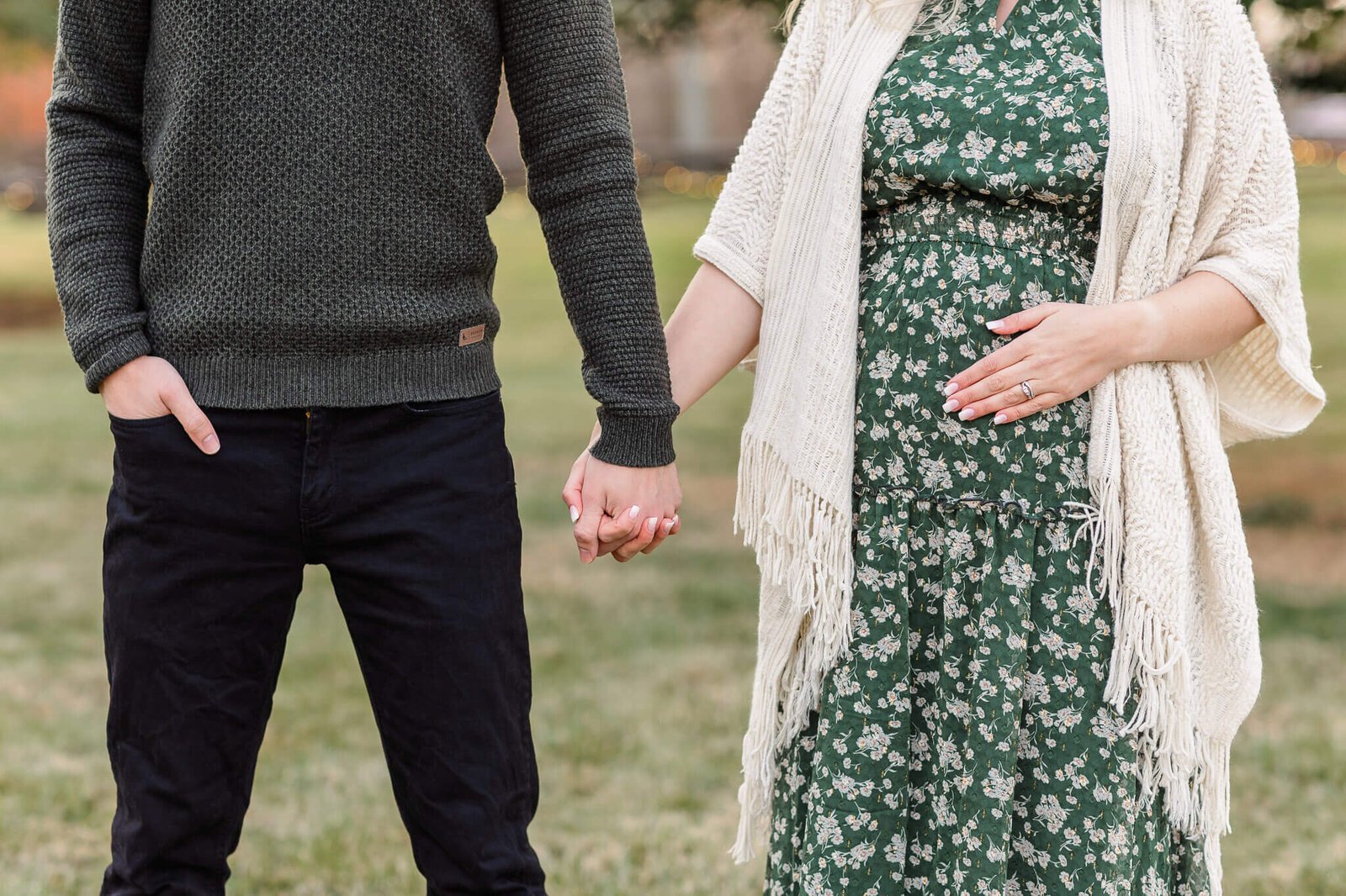 A close-up of a couple holding hands and holding mom's pregnant belly.