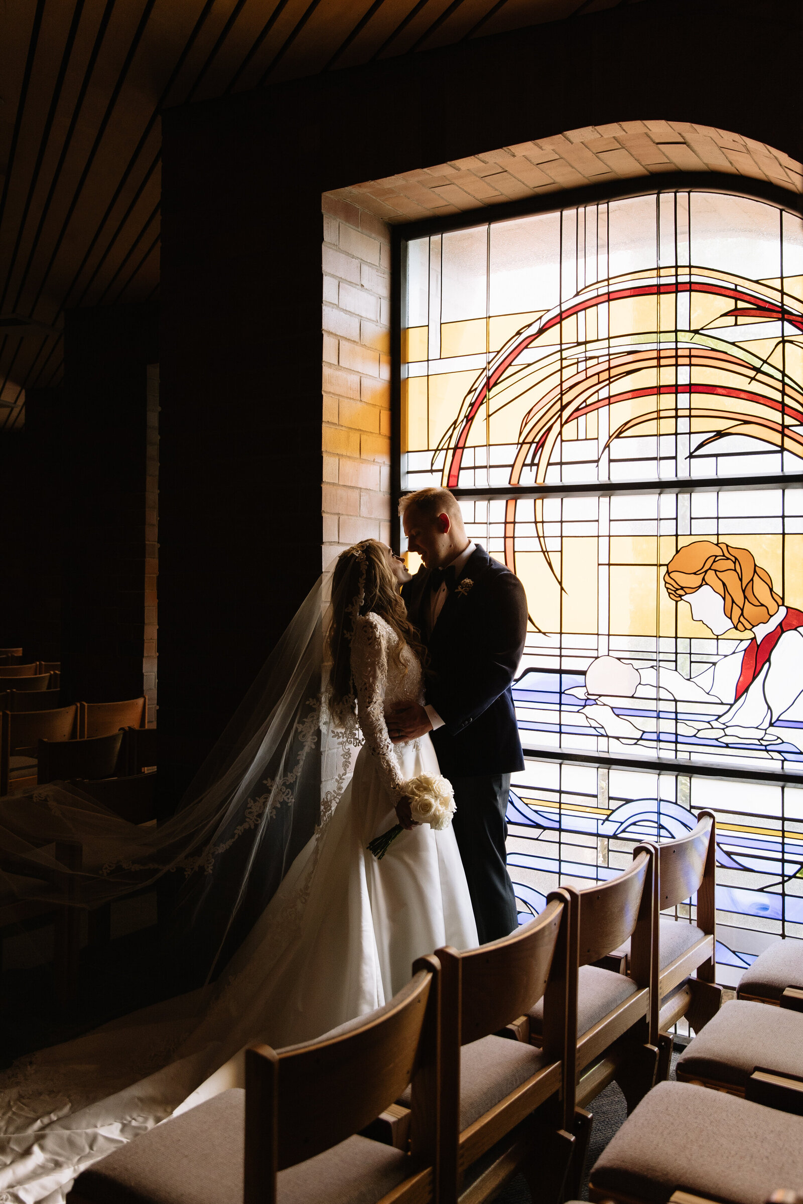 Moody photo of bride and groom posing in front of Catholic Church stained glass windows in Boise, Idaho