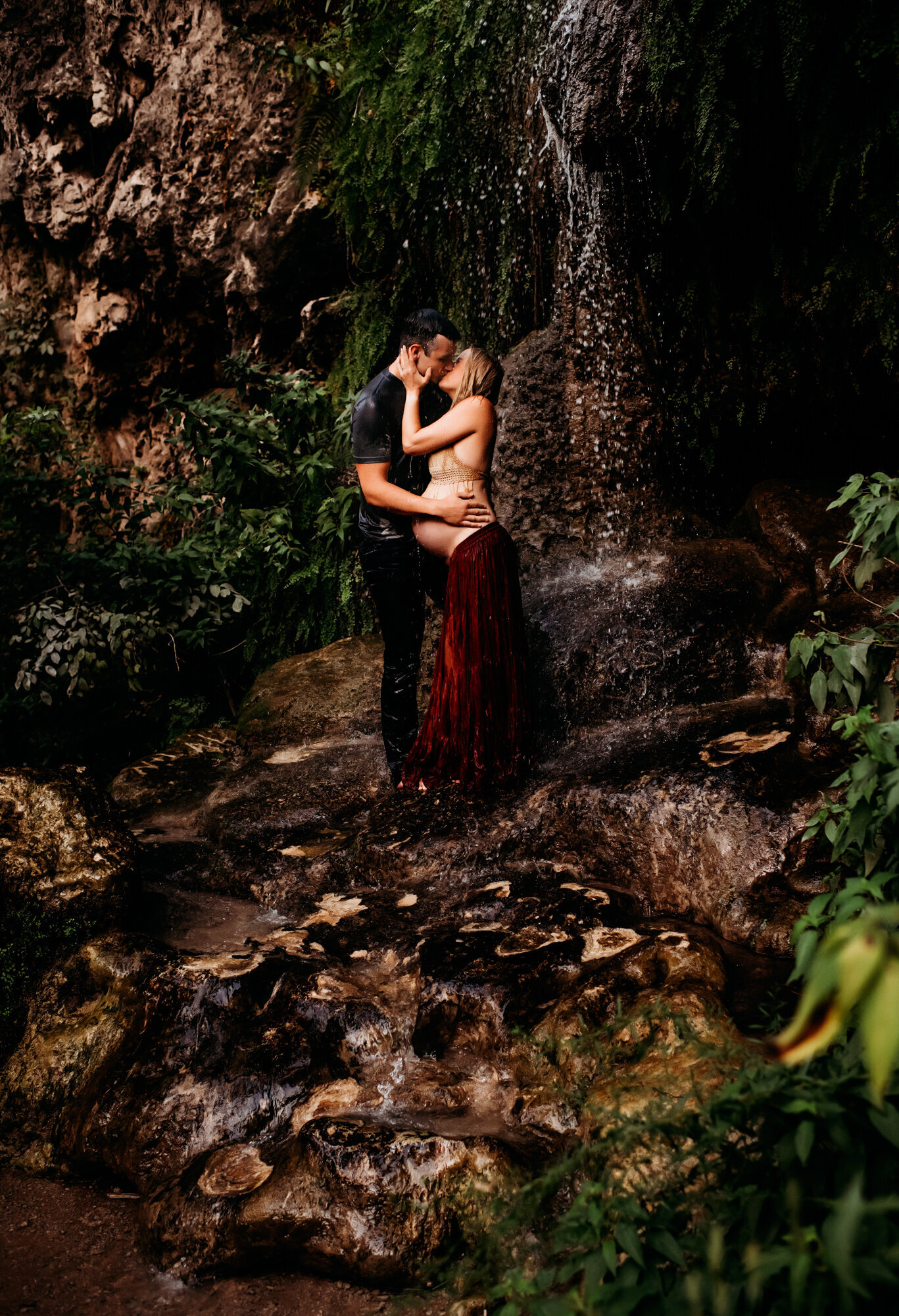 Maternity Photographer, Pregnant woman with in a skirt and woven top kissing under a waterfall.