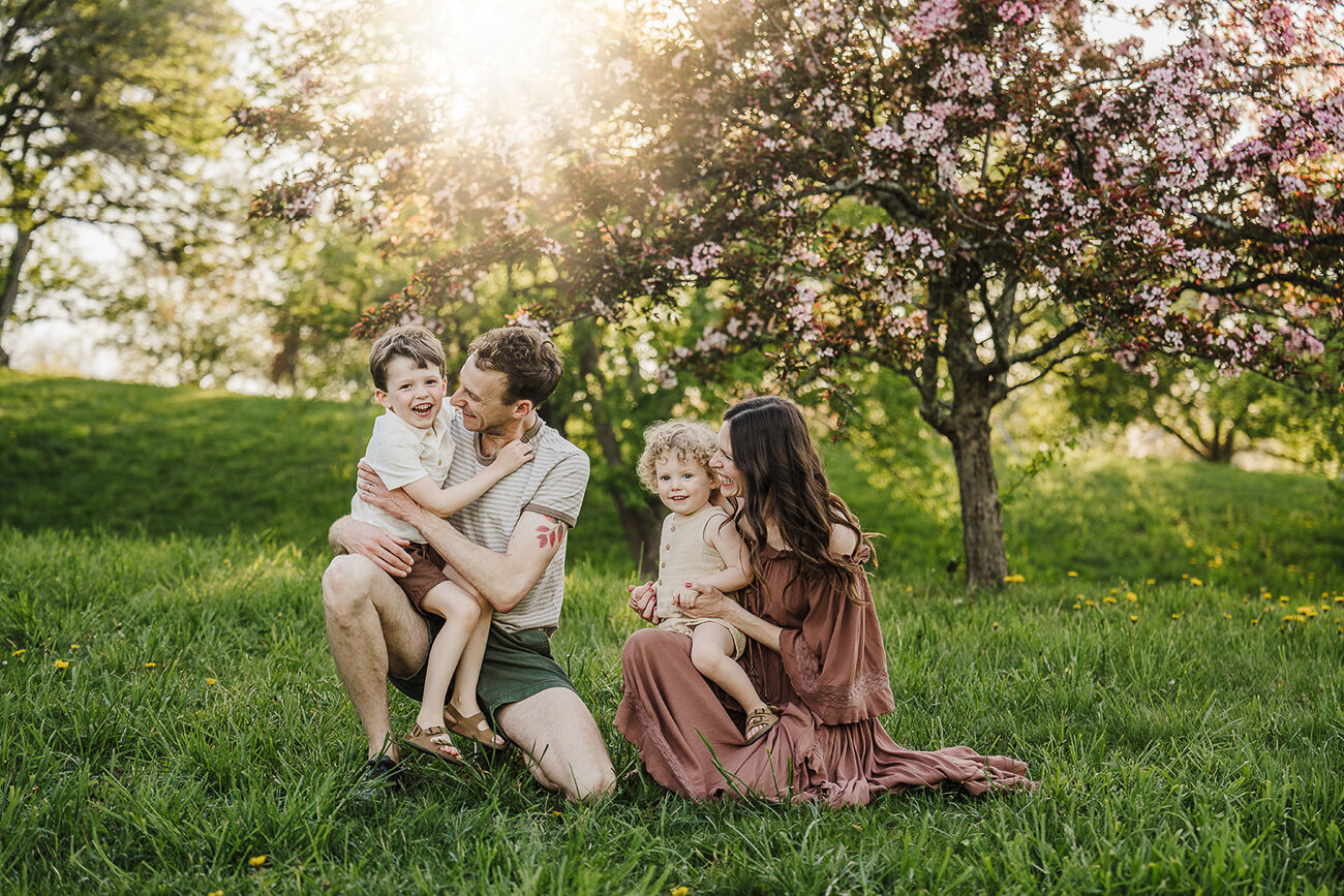 family with two sons laughs together under pink apple blossom trees