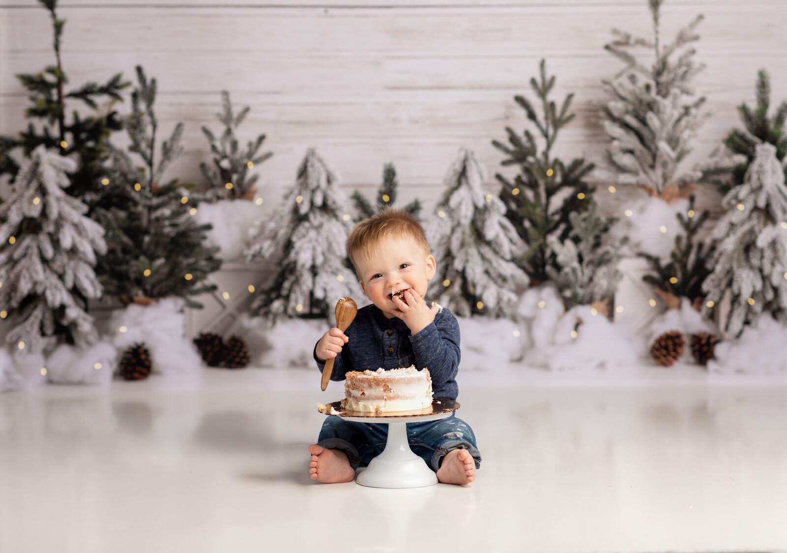one year old boy in blue shirt eating cake for first birthday photoshoot