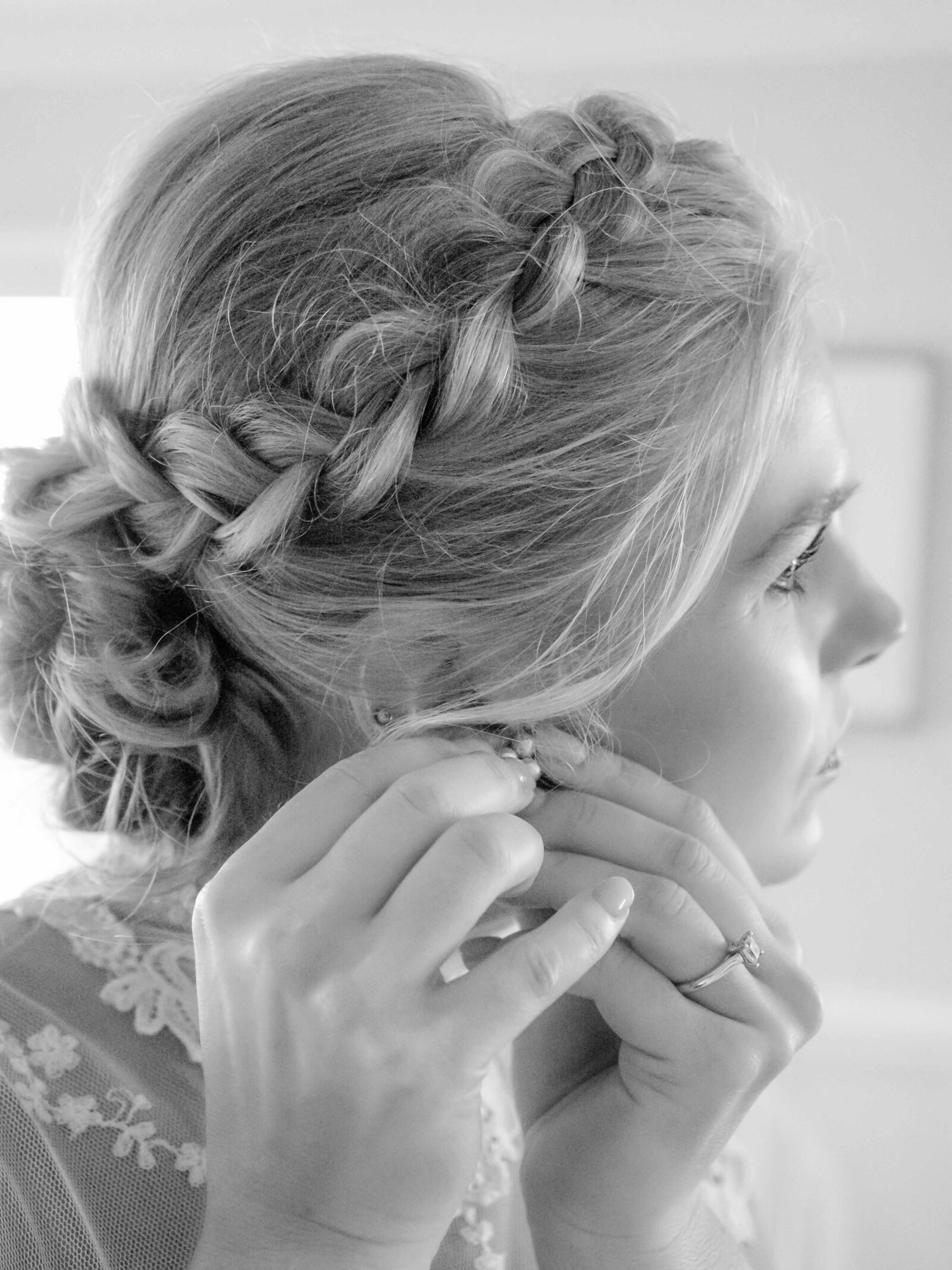 A bride adjusts her diamond earrings in a soft braided hairstyle, captured in a bridal suite during a Wrightsville Beach, NC wedding, highlighting authentic preparation moments and timeless elegance.