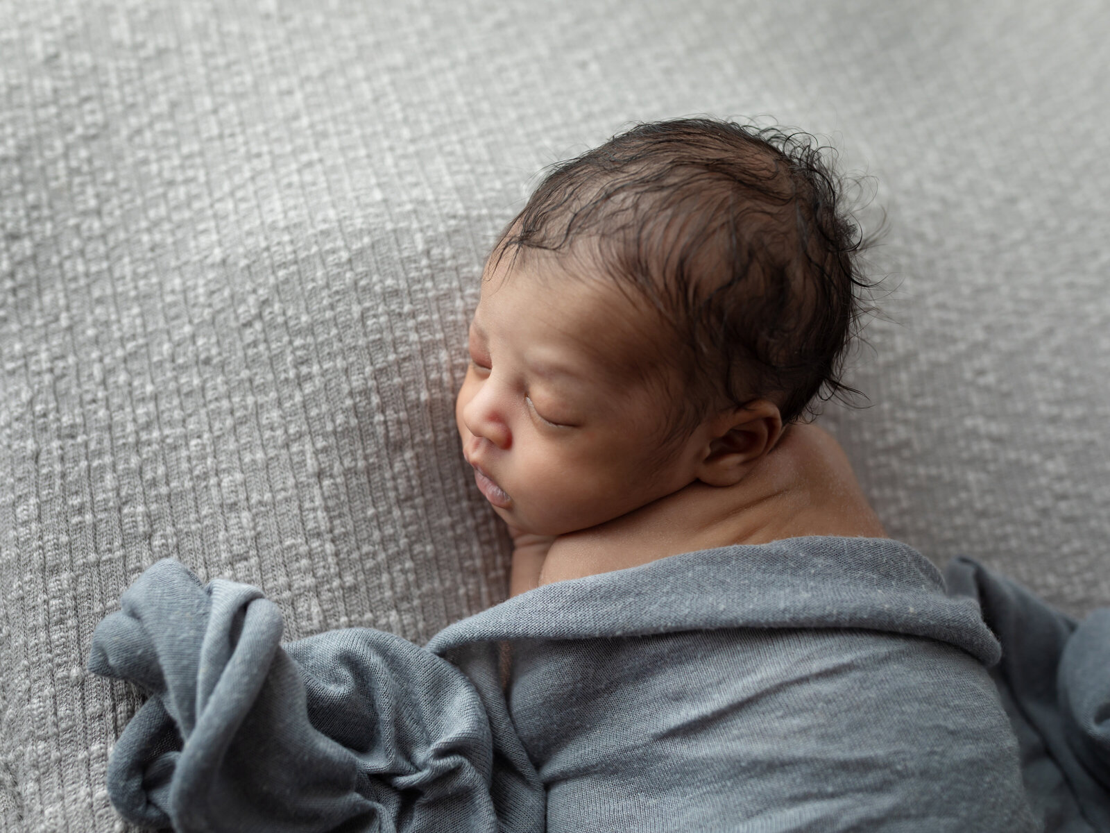 newborn baby boy posed on gray fabric for studio portraits 