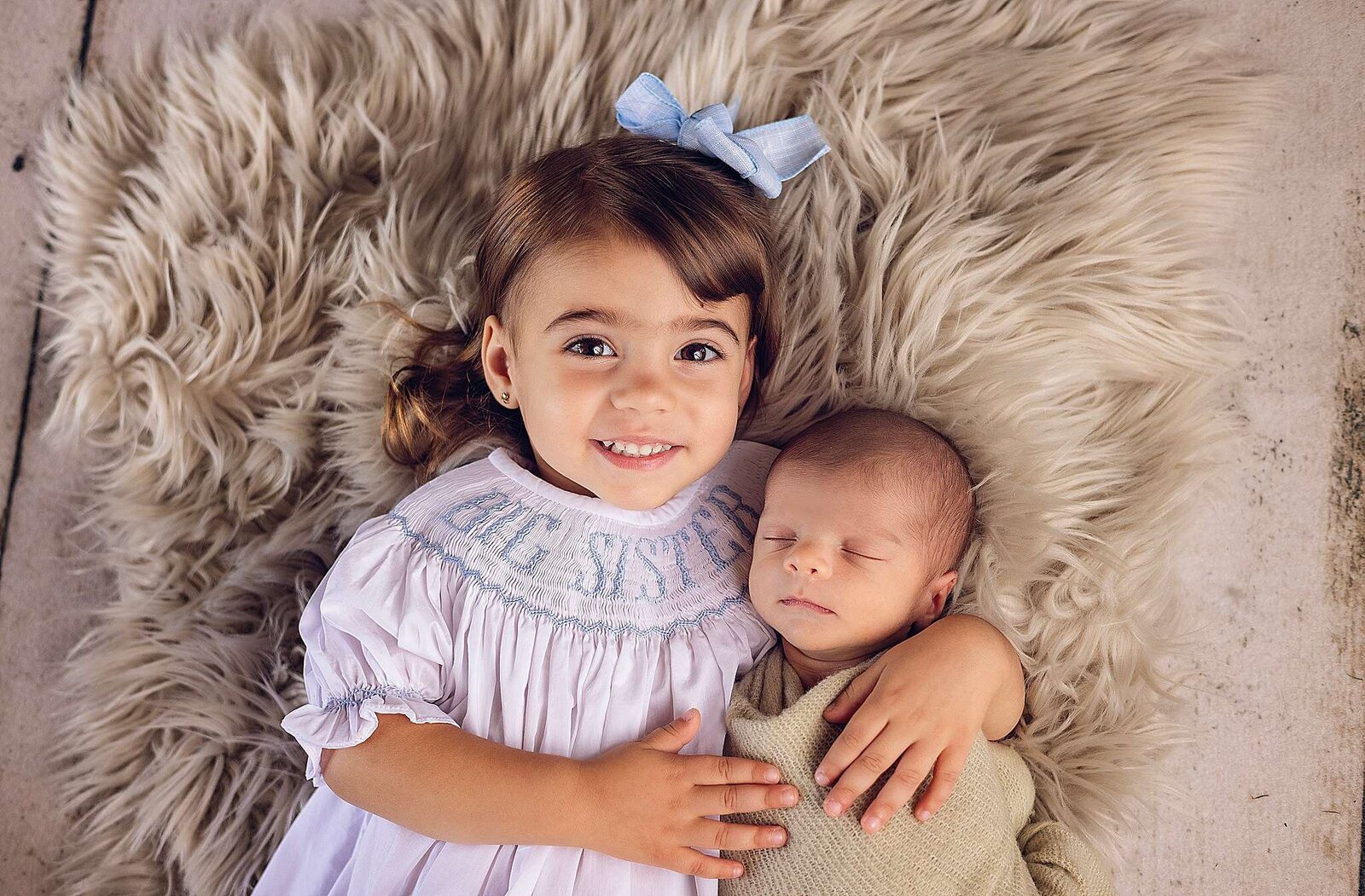 A little girl and boy relax together on a soft, furry rug during a cozy in-home newborn photography session in Orlando, Florida.