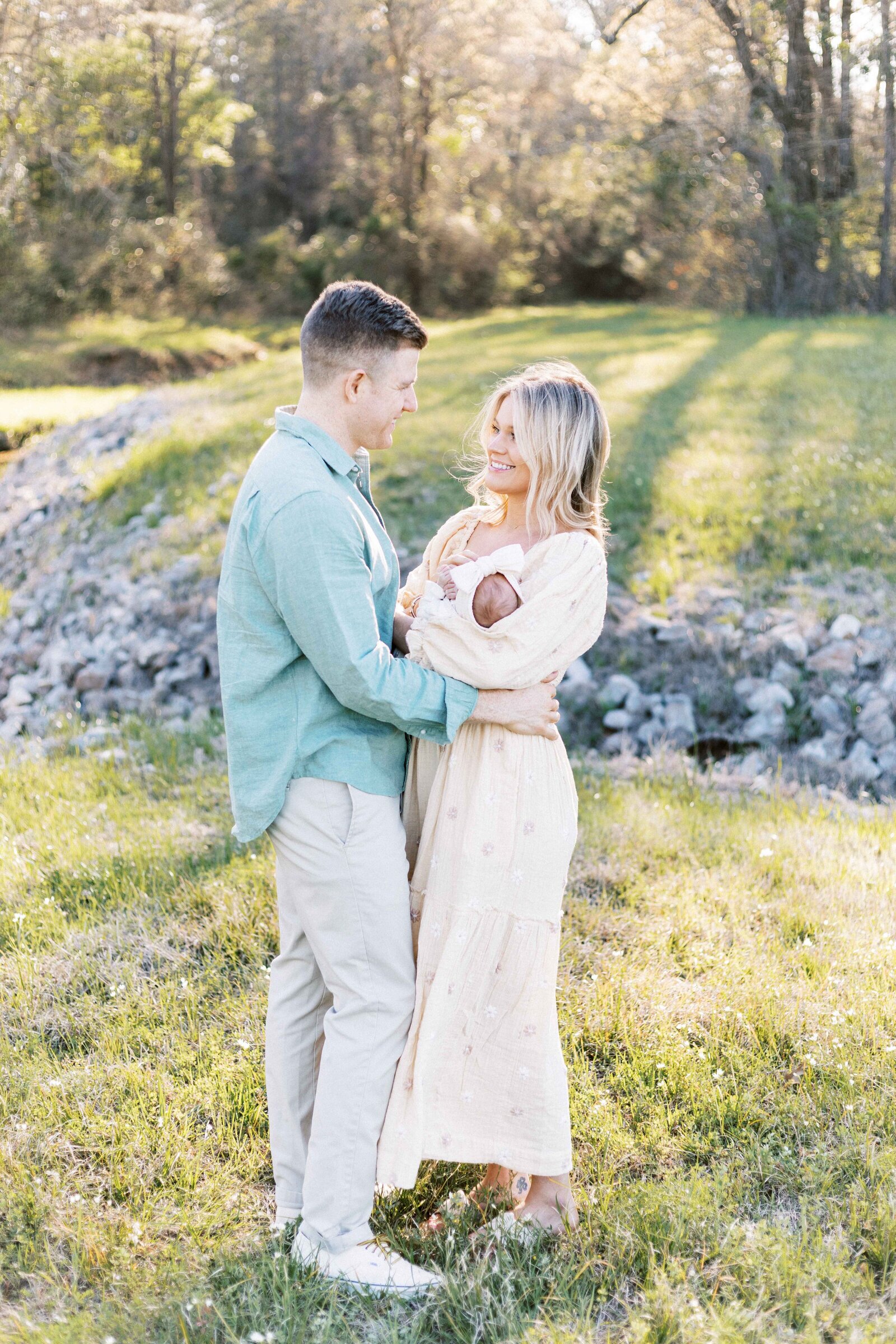 parents holding baby and looking at each other during outside newborn photos in peoria illinois 