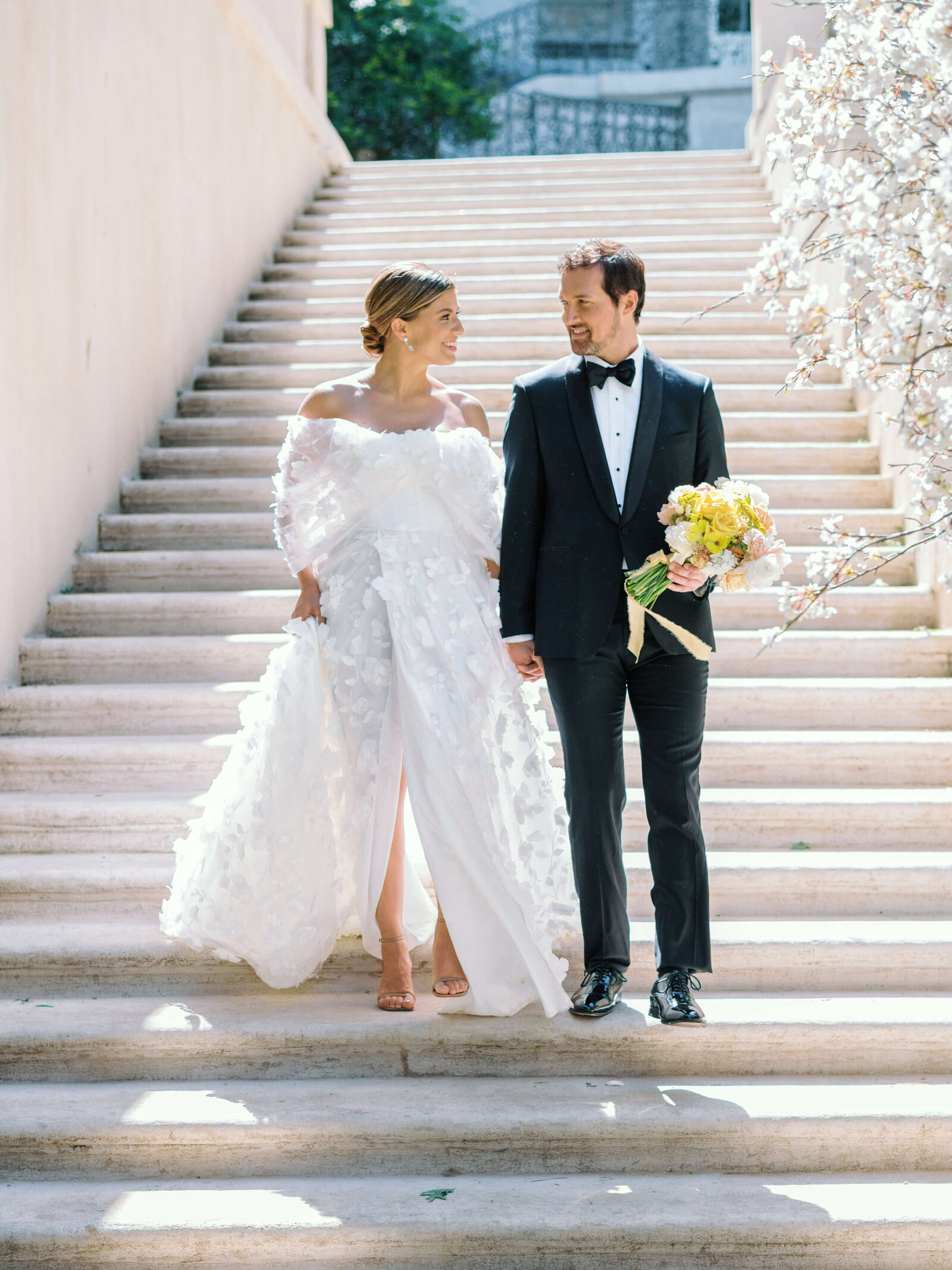 A newly married couple walks down the white stone steps during their wedding photos