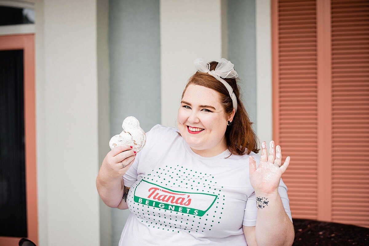 Social influencer wearing a Disney shirt and smiling at camera as she eats Disney beignets