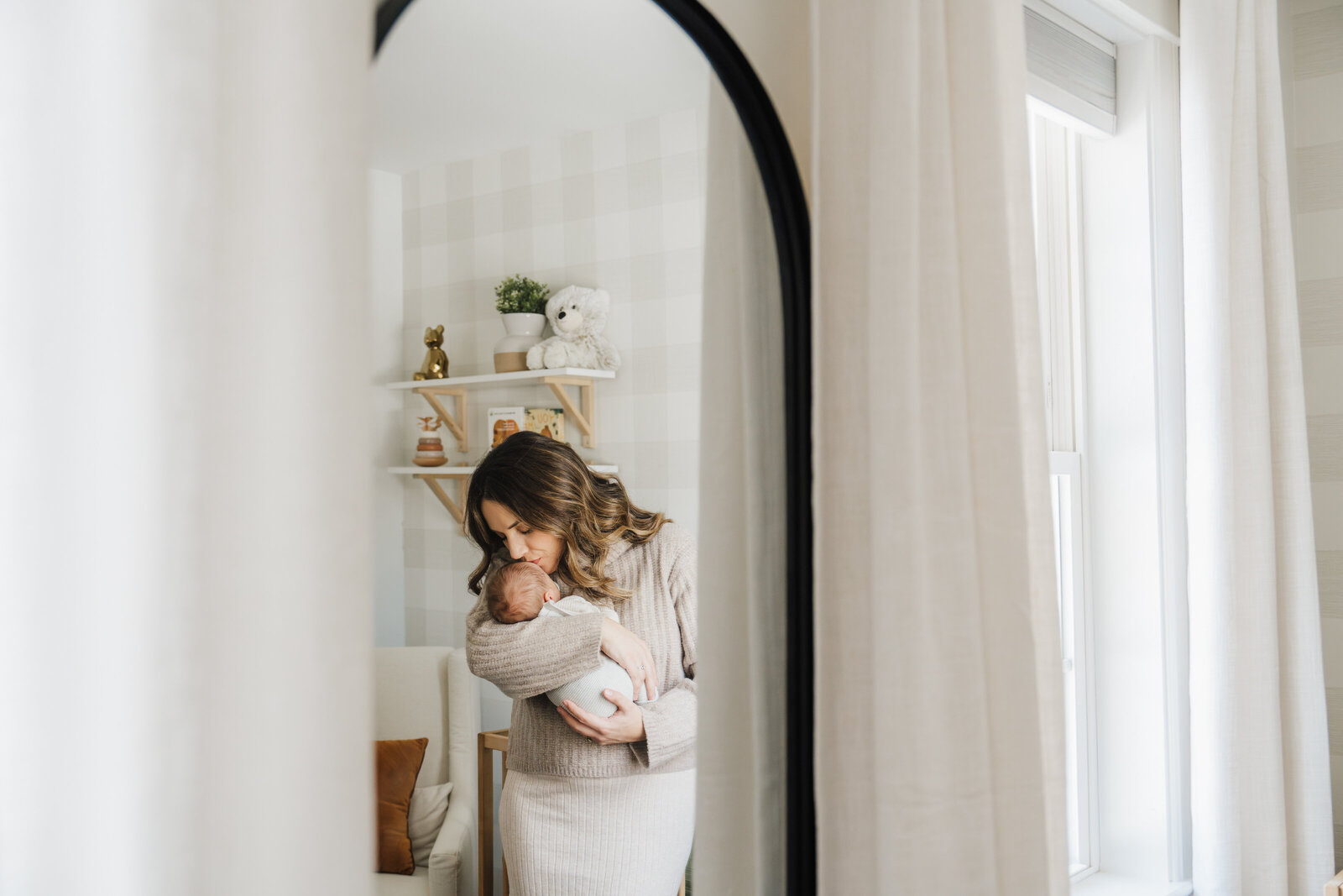 mother kisses infant son reflected in nursery mirror