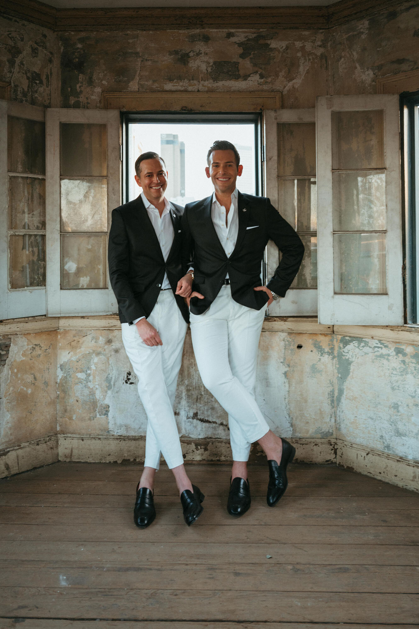 two grooms standing in  front of shuttered windows