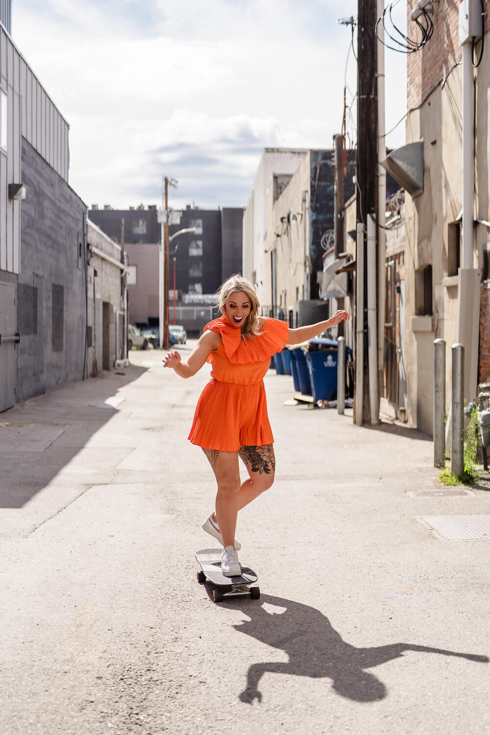 Young woman in orange jumper riding a skateboard in a downtown alleyway