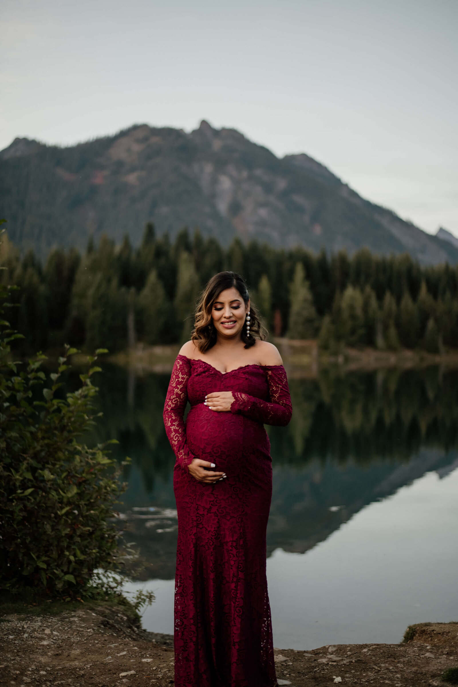 Mother standing holding baby bump with mountains behind her.