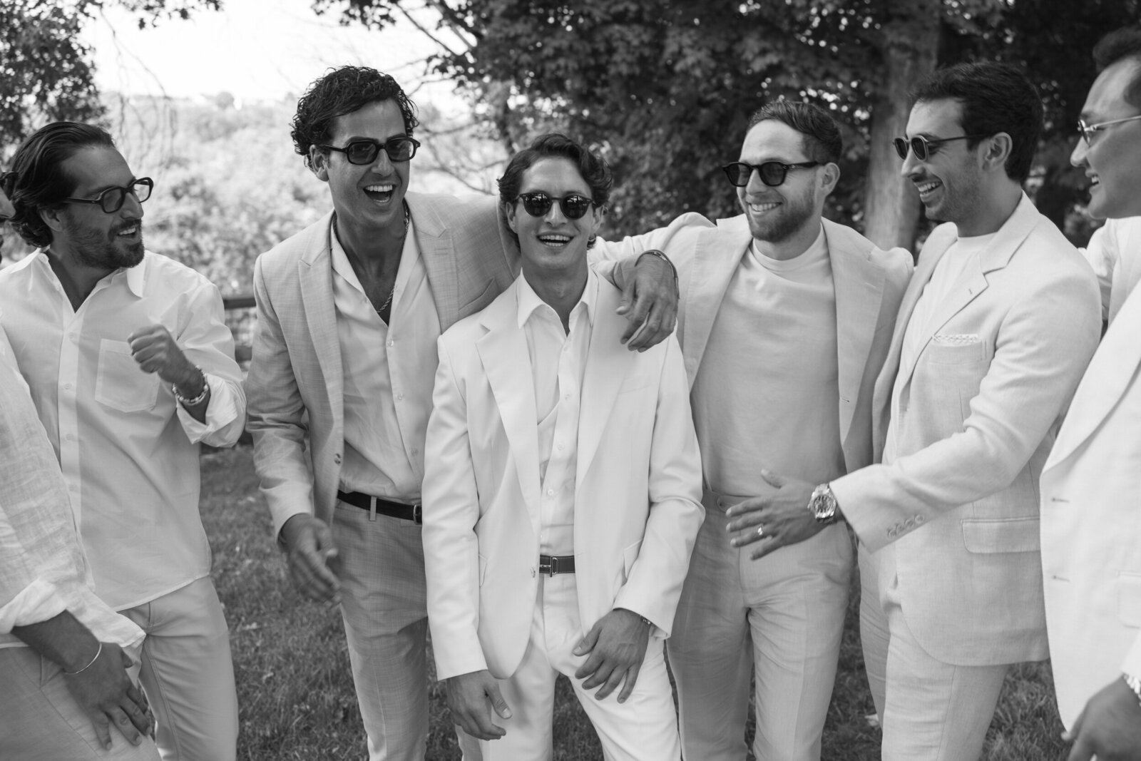 Candid black & white groomsman group photo laughing with arms around groom 