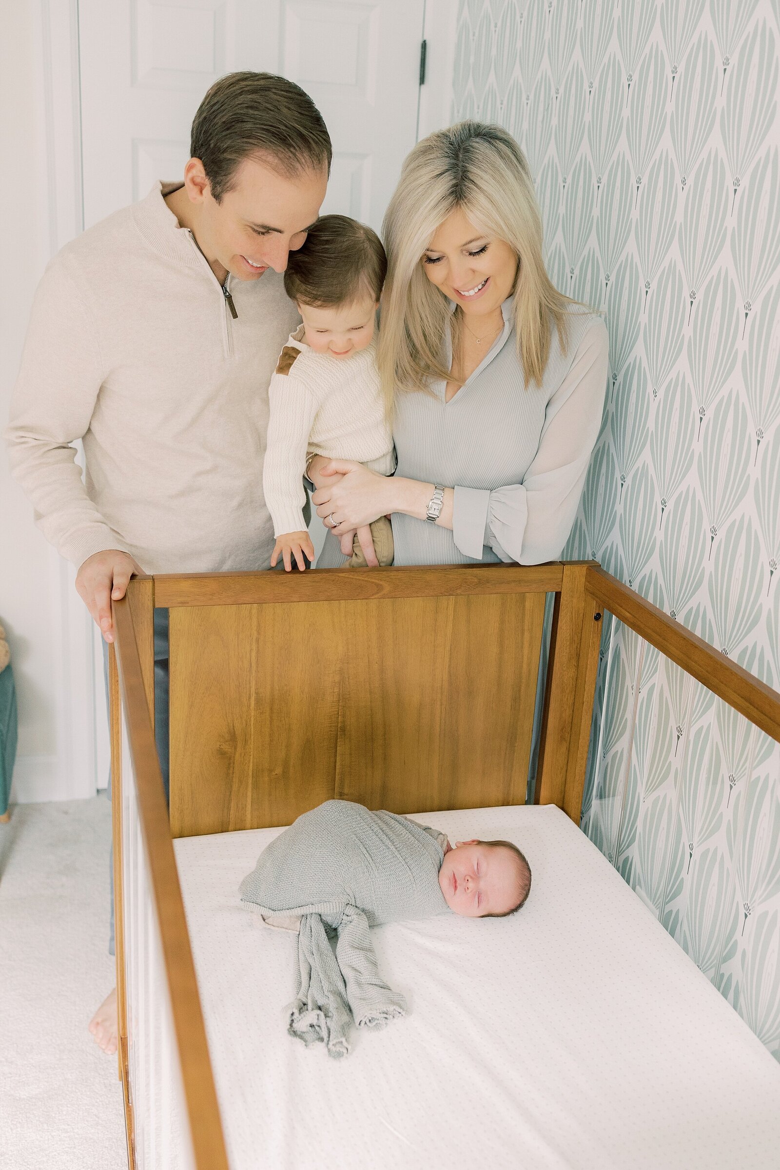 parents and big brother looking at sleeping baby in crib Newborn Photography West Chester PA