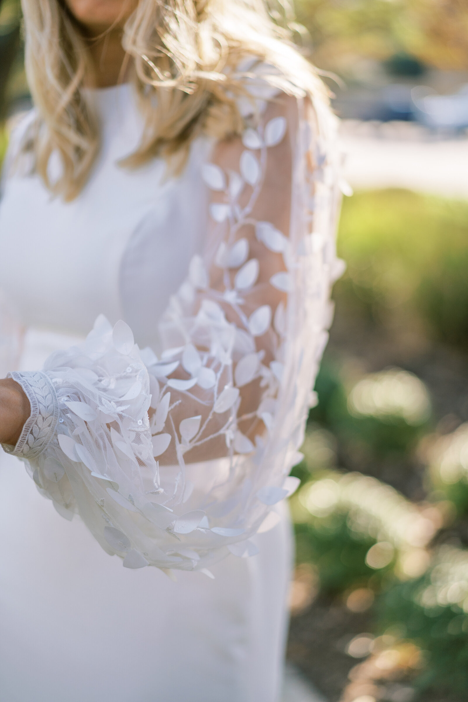 Bride in a white wedding gown with petals on the sleeves outdoors.