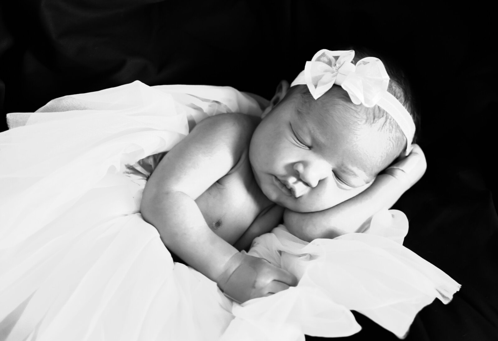 black and white photo of a sleeping newborn baby girl with a bow on her head photographed by Millz Photography in Greenville, SC