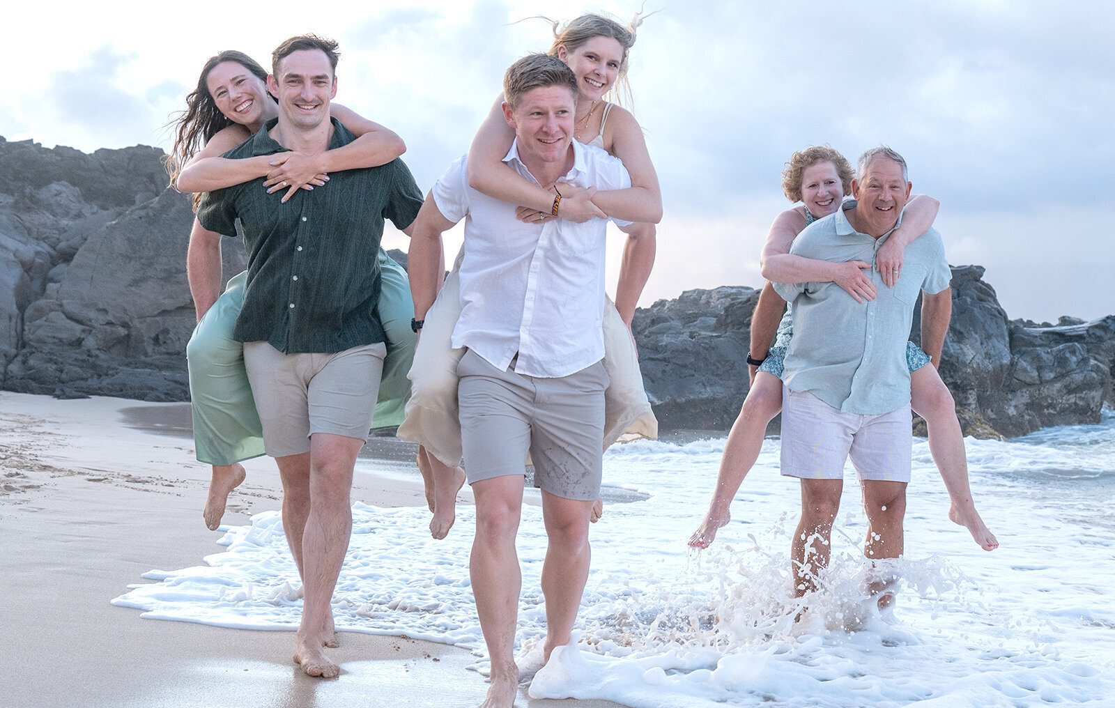three couples piggy back riding each other on the beach in Oahu for their family portrait photo shoot.