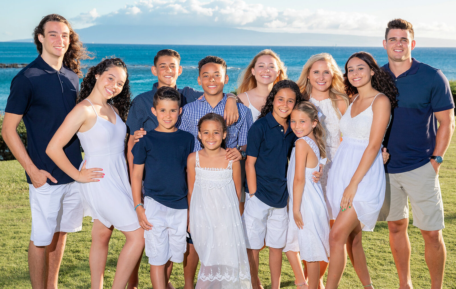 Family portrait  of 12 people on the grass over looking the beach in Oahu