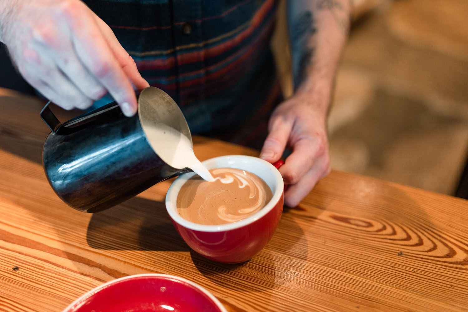 person pouring steamed milk into a mug of coffee