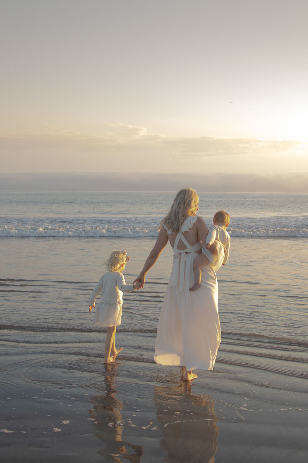 Mother walking with her two children along the beach at sunset
