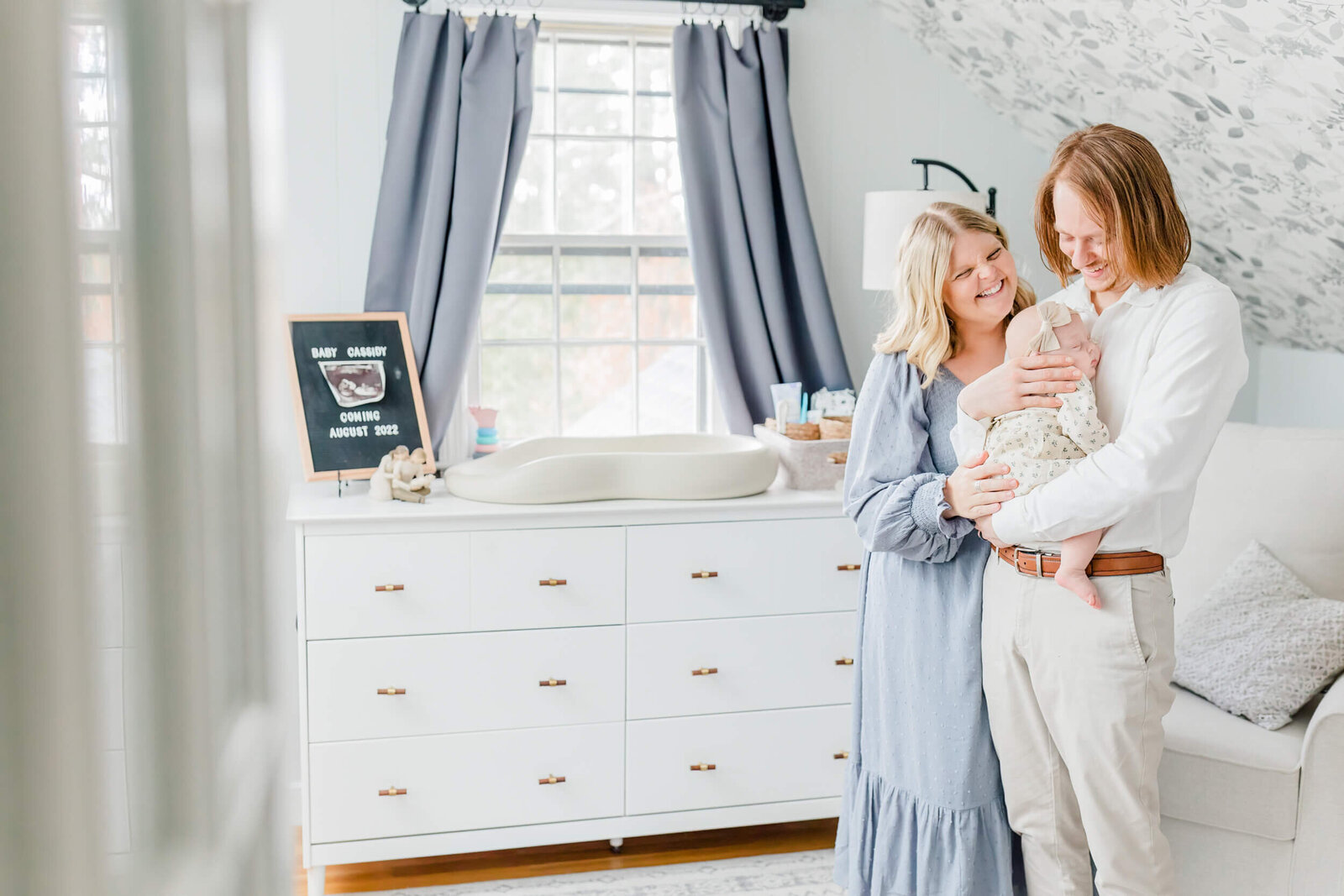 Dad holds newborn and smiles at her with mom