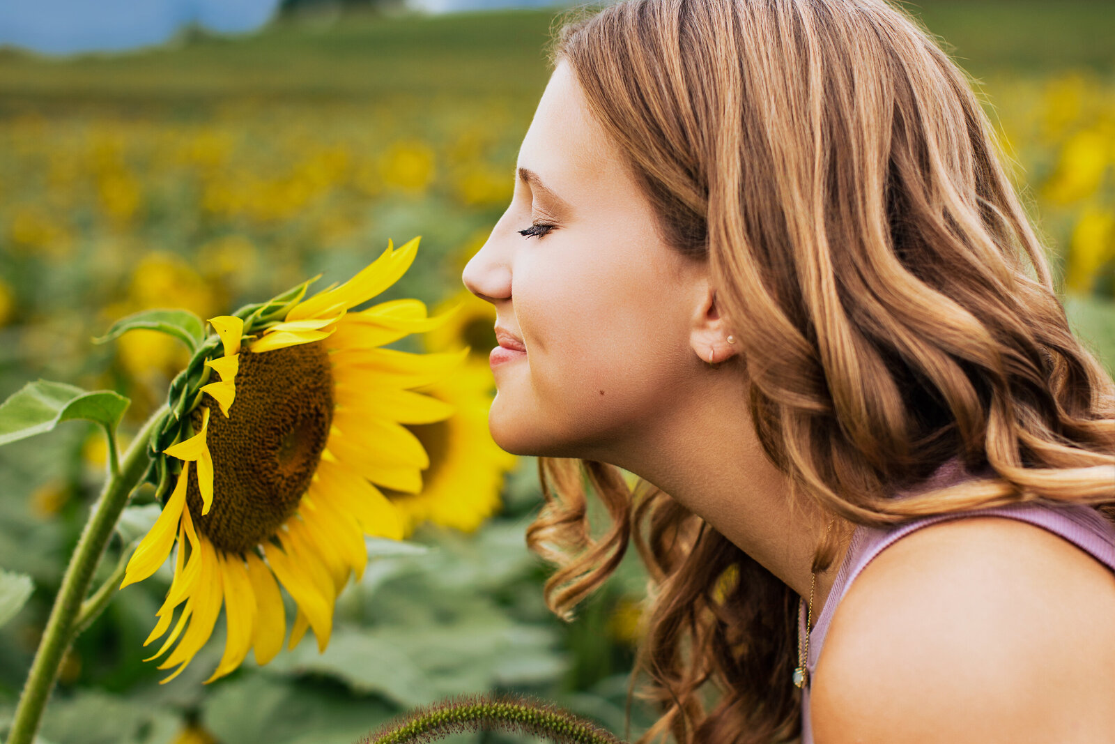 A pretty brown haired girl leans into smell a sunflower close-up in the senior Picture.
