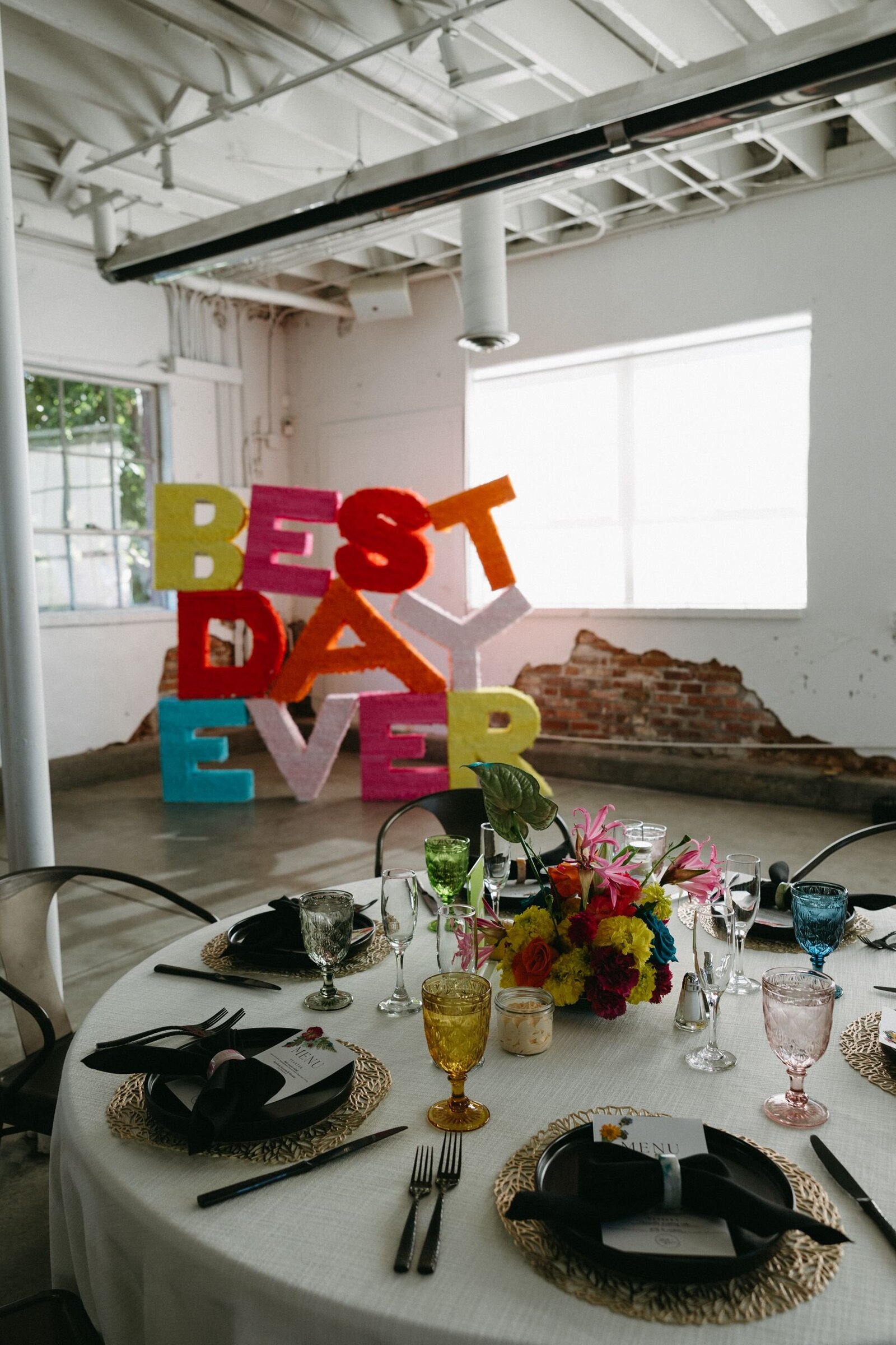 Pinata style letters spelling Best Day Ever sit in the corner of a wedding venue