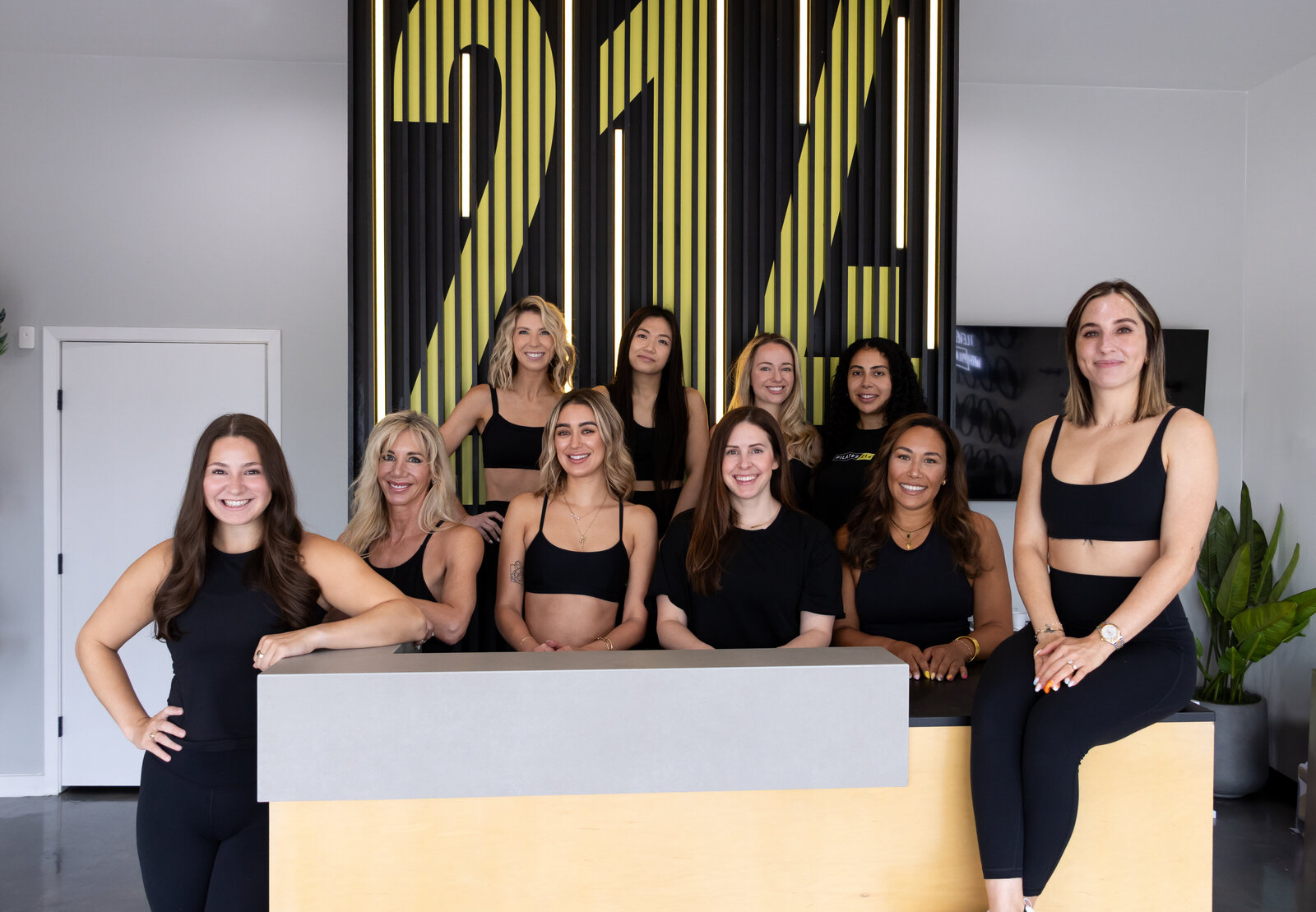 Group of Pilates214 Pilates instructors standing in front of neon I Leveled Up with Pilates214 sign in Dallas studio.