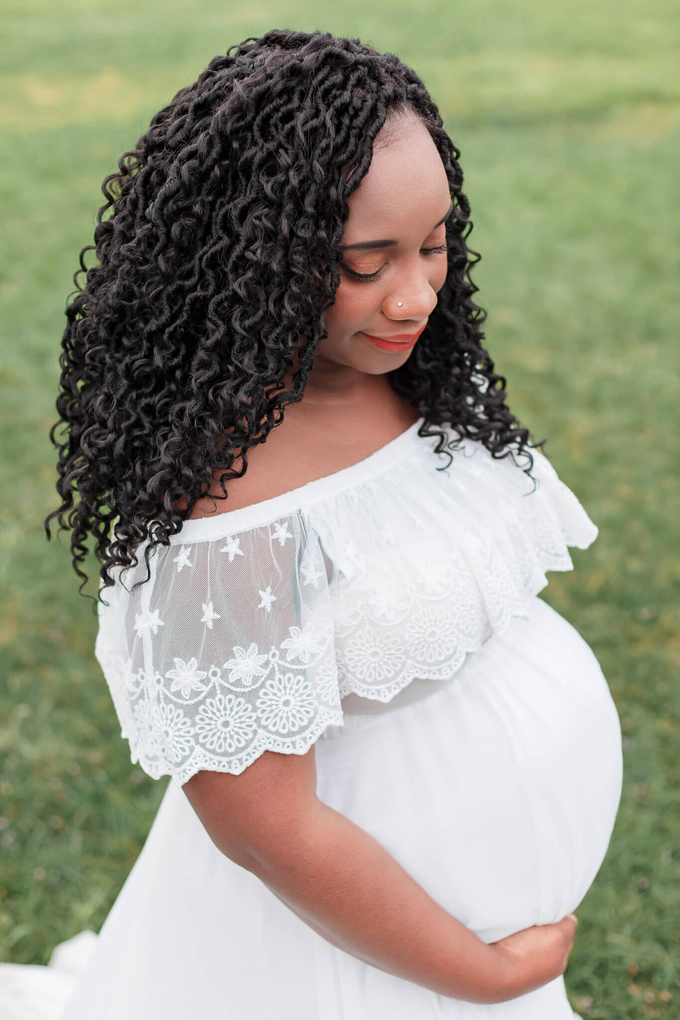 A pregnant woman in a white dress hugging her pregnant belly.