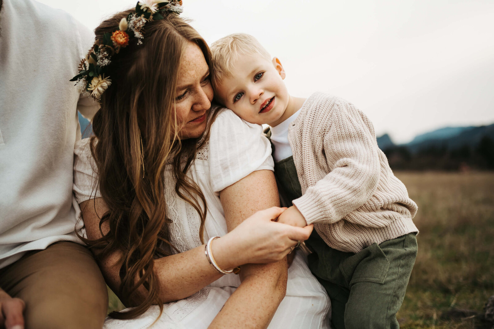 Mom holding her toddler's hand while sitting down on a field